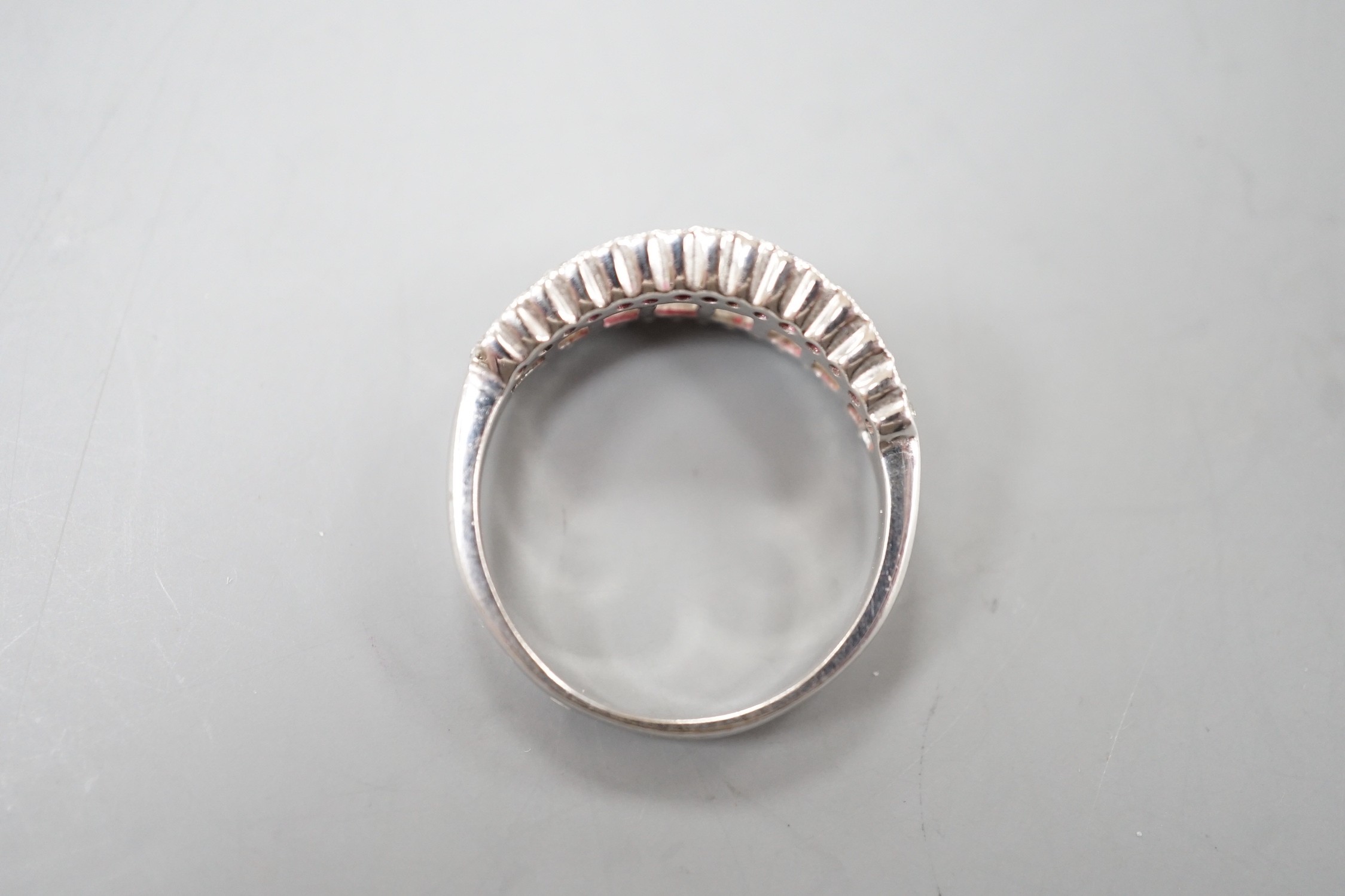 A modern white metal, graduated baguette cut diamond set half hoop ring, with diamond chip borders, size O, gross weight 5 grams.